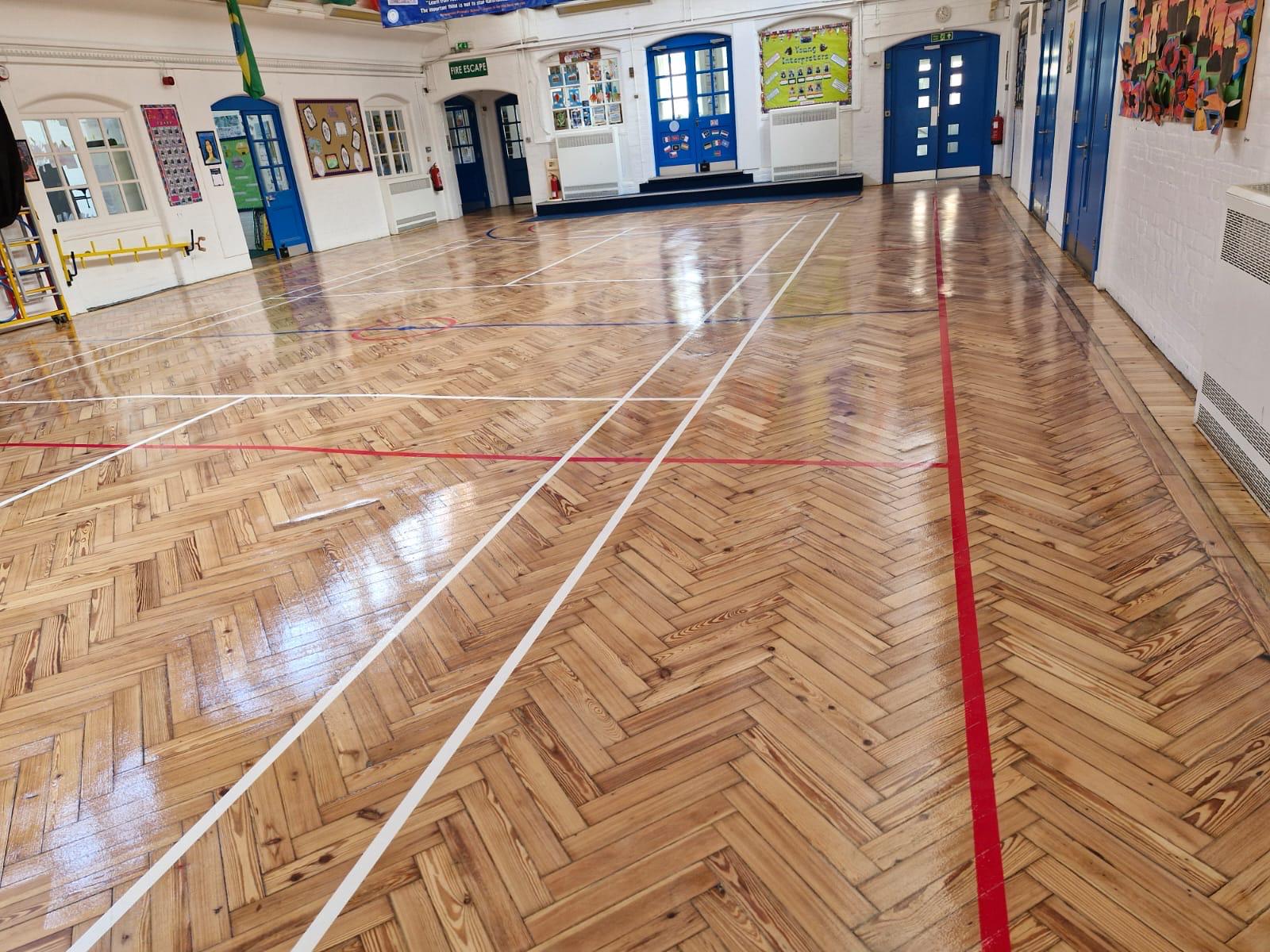 Freshly refinished school hall parquet floor with crisp white and red court markings, gleaming after professional school hall sanding.