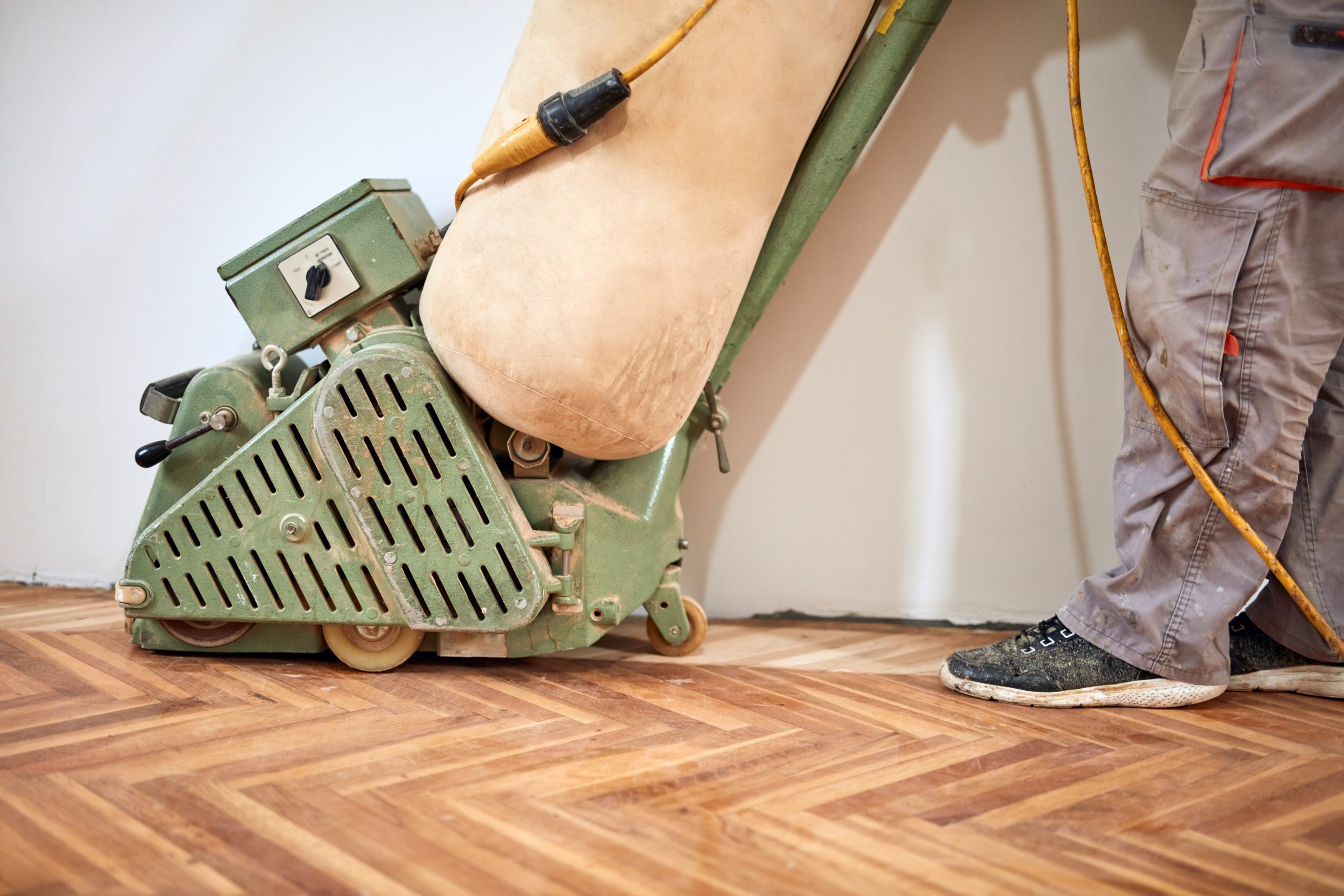 Close-up of a drum floor-sander gliding over a herringbone parquet surface during professional school hall sanding.